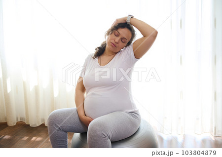 Gravid expectant woman, future mom expecting baby, practicing prenatal stretching exercising on fit ball. Sport. Fitness. Active healthy lifestyle in pregnancy time for easy childbirth and pain relief 103804879
