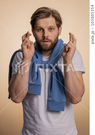 Young man crossed fingers looking at camera asking for good luck news dreaming about win victory Young man crossed fingers looking at camera asking for good luck news dreaming about win victory 103805354