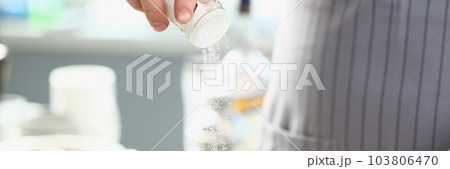 Cook pours salt into pan in kitchen 103806470