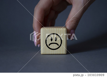 Sad smile symbol. Sad smile on wooden cube. Businessman hand. Beautiful grey background. Business and Sad smile concept. Copy space. 103810909