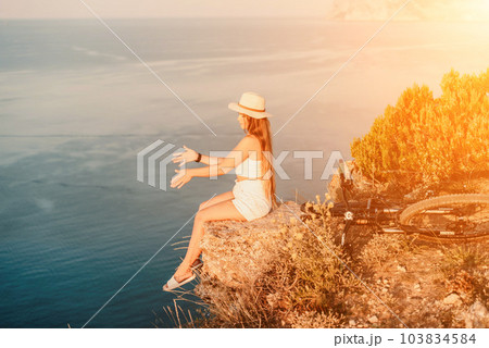 A woman cyclist on a mountain bike looking at the landscape of mountains and sea. Adventure travel on bike. A woman cyclist on a mountain bike looking at the landscape of mountains and sea. Adventure travel on bike. 103834584