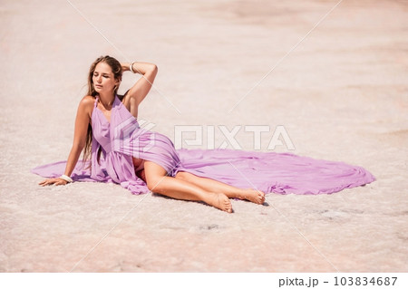 A woman in a pink dress sits on the salty shore of a pink lake and poses for a souvenir photo, creating lasting memories. 103834687