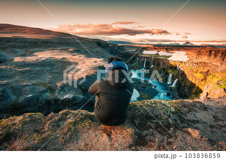 Traveler man sitting on edge of mountain with Sigoldugljufur waterfall on summer in Icelandic Highlands 103836859