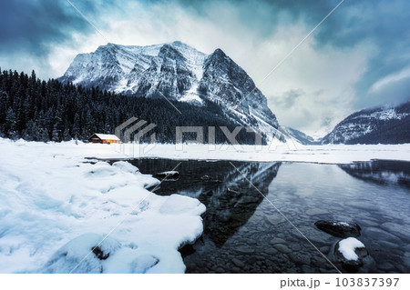 Scenery of Lake Louise with wooden cottage glowing and rocky mountains with snow covered in winter at Banff national park 103837397
