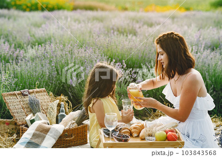 Mother with little daughter on lavender background. Beautiful woman and cute baby playing in meadow field. Family in a picnic. 103843568