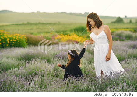 Mother with little daughter on lavender background. Beautiful woman and cute baby playing in meadow field. Family holiday in summer day. Mother with little daughter on lavender background. Beautiful woman and cute baby playing in meadow field. Family holiday in summer day. 103843598