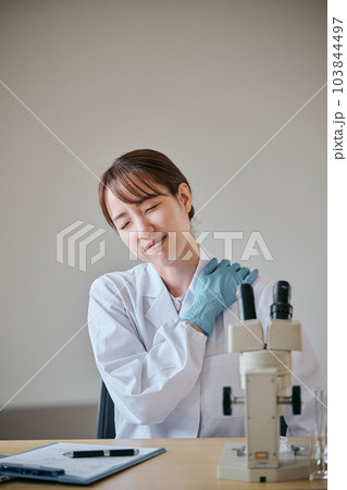 肩が凝り手で押さえる白衣の若い女性 103844497