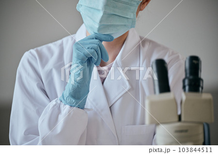 デスクで顎に手を当てて考え事をする白衣の若い女性 103844511