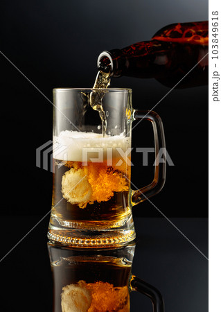 Pouring beer from a bottle into a mug. Pouring beer from a bottle into a mug. 103849618