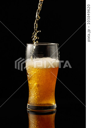 Pouring beer into a glass on a black reflective background. 103849620