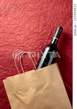 Paper shopping bag with a bottle of red wine on a textured red background. Paper shopping bag with a bottle of red wine on a textured red background. 103849637