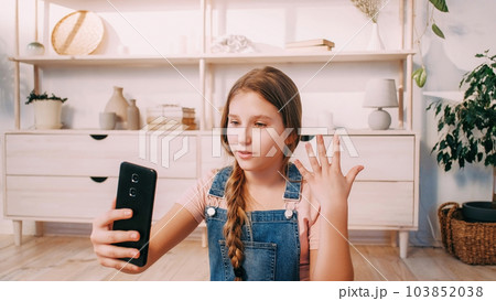 Video call. Child blogger. Online communication. Expressive confident girl speaking to smartphone camera gesticulating in light room at home. 103852038