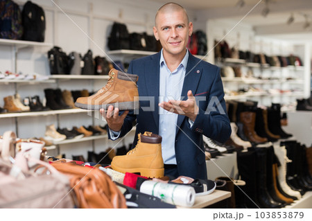 Male sales consultant offering demi-season mens boots in shoe store 103853879