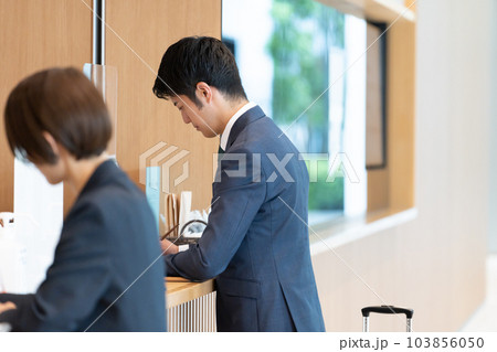 ホテルのフロントで手続きするビジネスマン（出張・予約） 103856050