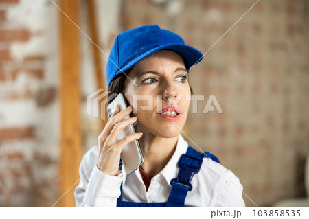 Woman builder using smartphone while standing in renovated room 103858535