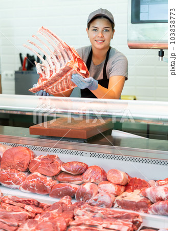 Butcher shop salesgirl holding slab of raw beef ribs for tomahawk steak Butcher shop salesgirl holding slab of raw beef ribs for tomahawk steak 103858773
