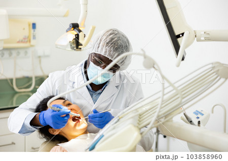 Male dentist using tools for tooth repairing on woman patient 103858960