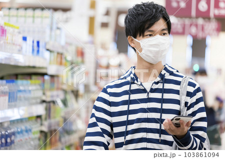 スーパーでスマホを見ながら買い物をするマスク姿の若い男性 スーパーでスマホを見ながら買い物をするマスク姿の若い男性 103861094