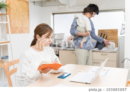 夫に子守を分担してもらって、メモを取りながら在宅ワークする妻 103865897