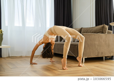 Woman exercising at home doing full back arch exercise Woman exercising at home doing full back arch exercise 103866595