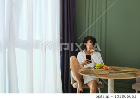 Woman in bathrobe using smartphone and eats grapes after taking bath Woman in bathrobe using smartphone and eats grapes after taking bath 103866663