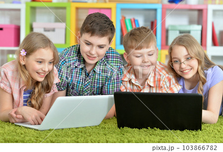 Children lying on floor with green carpet and looking at modern laptops 103866782