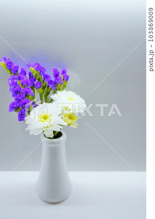 明るく照らされたホワイトバックに白い陶器の花立に飾られた白い小菊と紫のスターチスの仏壇用の花、縦 明るく照らされたホワイトバックに白い陶器の花立に飾られた白い小菊と紫のスターチスの仏壇用の花、縦 103869009