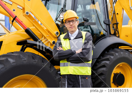 Engineer with a digital tablet stands next to construction excavators 103869155