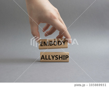 Embody Allyship symbol. Concept word Embody Allyship on wooden blocks. Beautiful grey background. Businessman hand. Business and Embody Allyship concept. Copy space 103869931