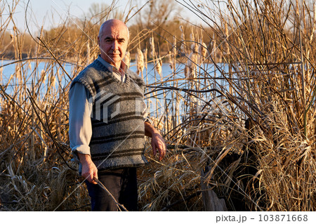 Elderly cheerful pensioner in a picnic in nature among the reeds on the lake 103871668