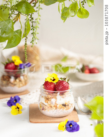 Yogurt with granola, edible flowers and strawberries, vertical light frame, selective focus. Yogurt with granola, edible flowers and strawberries, vertical light frame, selective focus. 103871708