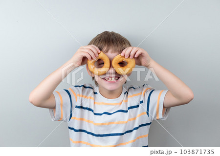 The blond boy looks through the donuts like through glasses. Portrait of a smiling child with donuts 103871735
