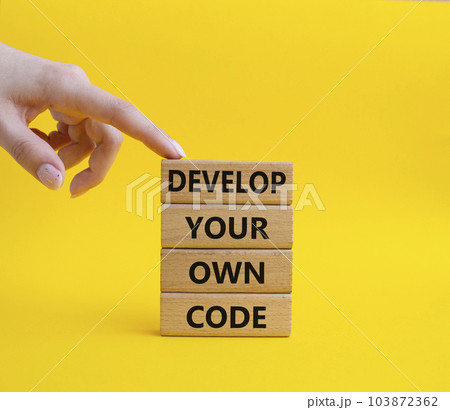 Develop your own code symbol. Concept words Develop your own code on wooden blocks. Beautiful yellow background. Businessman hand. Business and Develop your own code concept. Copy space. 103872362