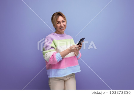 blond smiling young woman in casual outfit holding a smartphone in her hands on a purple background blond smiling young woman in casual outfit holding a smartphone in her hands on a purple background 103872850