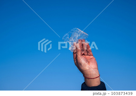 man's hand holds a piece of ice in winter against a blue sky 103873439
