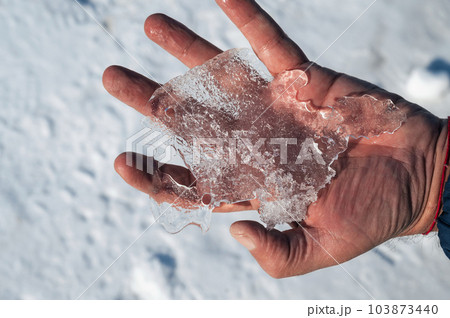 man's hand holds a piece of ice in winter 103873440