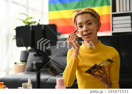 Charming young gay man blogger recording make up tutorial, live streaming at home. LGBTQ lifestyle, influencer, blogger Charming young gay man blogger recording make up tutorial, live streaming at home. LGBTQ lifestyle, influencer, blogger 103875531
