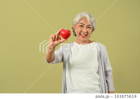 Beautiful senior woman holding a red heart and smiling to camera. Cardiology, medical and healthcare concept 103875619