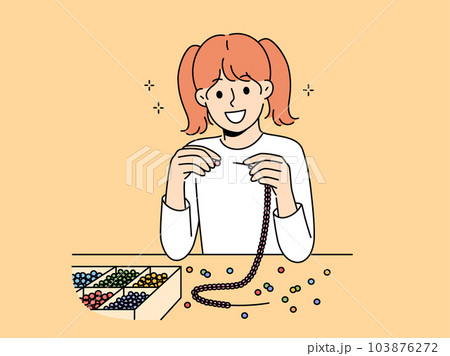 Little girl weaves beaded jewelry sitting at table and creating handmade necklace or bracelet 103876272