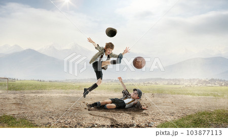 Little boys, children in retro style clothes playing football outdoors on a daytime, falling on dirt, kicking ball in jump 103877113