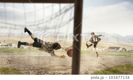 Two little boys, children in retro style clothes playing football outdoors on a daytime. Kicking ball into gate. Concentration Two little boys, children in retro style clothes playing football outdoors on a daytime. Kicking ball into gate. Concentration 103877138
