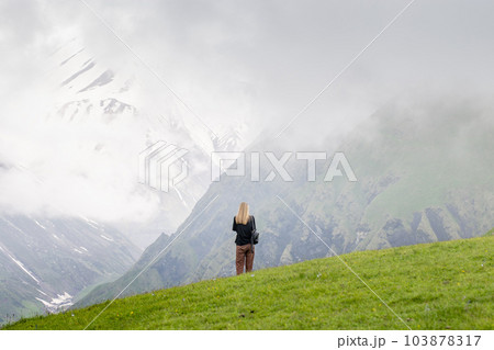 A young woman admires the majestic view of the panorama mountain landscape. A young woman admires the majestic view of the panorama mountain landscape. 103878317