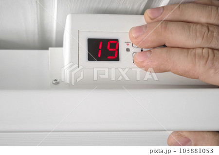 Man Lowering the Temperature on Electric Heater. Close Up. Person Adjusting Thermostat on Radiator to Save Energy due to Heating Cost Price Hike. Energy Saving. Celsius Units. Changing Heating. Man Lowering the Temperature on Electric Heater. Close Up. Person Adjusting Thermostat on Radiator to Save Energy due to Heating Cost Price Hike. Energy Saving. Celsius Units. Changing Heating. 103881053