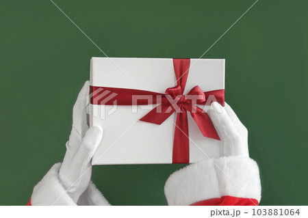Santa Claus Hand Holding Gift Box With Red Ribbon Isolated On Green Background. Close Up. Christmas Congratulation. Chroma Key Screen. Winter Present. Proposing product. Advertisement gesture. 4K 103881064