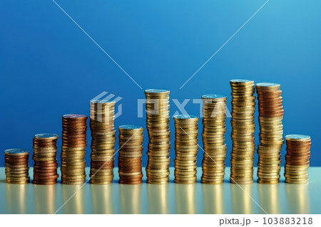 Stacks of coins of different heights depict a financial chart. Bank and finance. Investment, profit or gain. Selling money or treasury. Blue background with reflection. Copy space. 103883218
