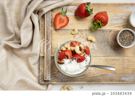 Glass jar of yogurt, nuts and strawberries on a wooden tray top view, copy space Glass jar of yogurt, nuts and strawberries on a wooden tray top view, copy space 103883439