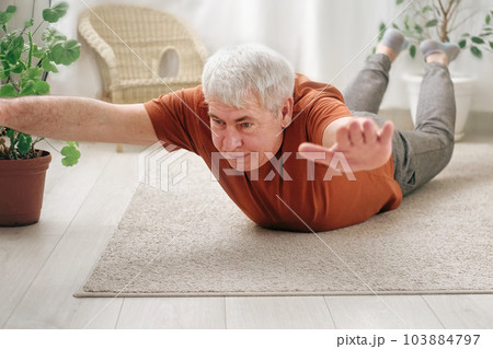 Happy smiling mature senior man doing exercises of gymnastics at home. Concept of healthy lifestyle, fitness, recreation, well being. Elderly male exercising training, stretching. Old man working out 103884797