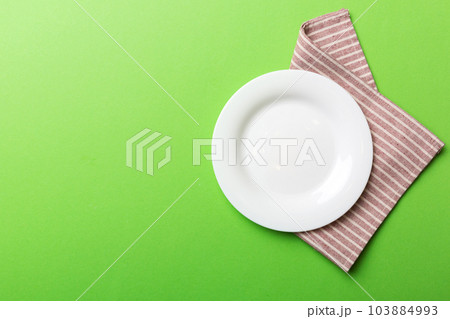 Top view on colored background empty round white plate on tablecloth for food. Empty dish on napkin with space for your design Top view on colored background empty round white plate on tablecloth for food. Empty dish on napkin with space for your design 103884993