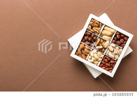 Various varieties of nuts lying in paper box on table background. Top view. Healthy food. Close up, copy space, top view, flat lay. Walnut, pistachios, almonds, hazelnuts and cashews Various varieties of nuts lying in paper box on table background. Top view. Healthy food. Close up, copy space, top view, flat lay. Walnut, pistachios, almonds, hazelnuts and cashews 103885035