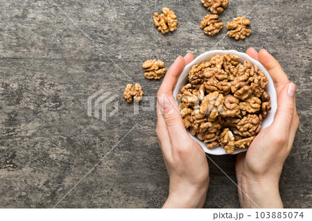 Woman hands holding a wooden bowl with walnut nuts. Healthy food and snack. Vegetarian snacks of different nuts 103885074